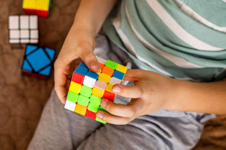 Closeup hands male teenager assembling Rubiks cube multicolored logical puzzle brainstormingのeditorial素材