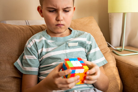 Portrait frowning male teenager brainstorming assembling Rubiks cube solving mind logic decisionのeditorial素材