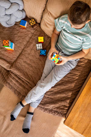 Top view male kid assembling multicolored Rubiks cube 4x4 relaxing sitting on couch