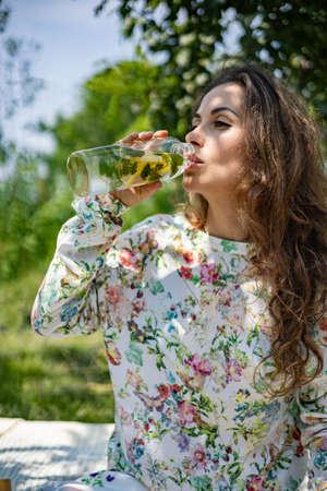 Portrait of beautiful woman posing lying on plaid at summer garden park. A book, fruit, a bag and a...
