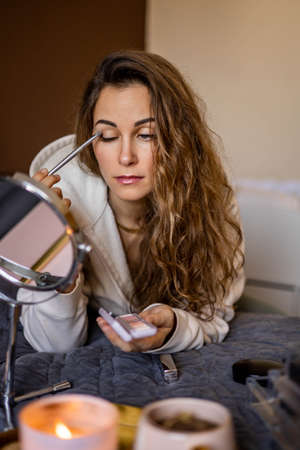 Beautiful female applying face tone powder foundation blush use brush looking at mirror makeupの写真素材