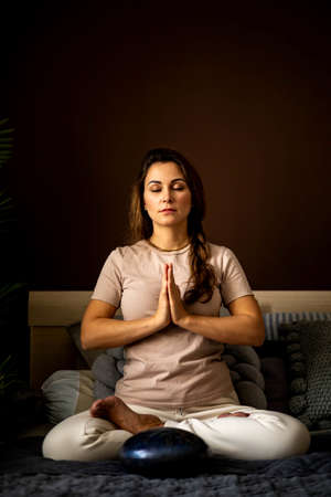 Relaxed yoga woman meditation in lotus position with hands namaste on bed at bedroomの写真素材