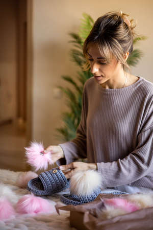 Portrait happy blonde woman art clothes designer creative ribbon yarn knitted slippers with pom pomの写真素材