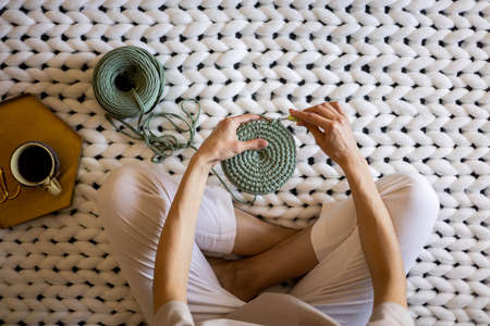 Top view creative woman knitting use ribbon yarn and crochet needle sitting on warm white plaid