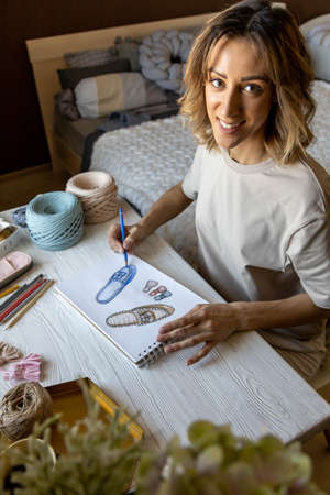 Creative woman clothes and shoes designer drawing colored sketch of slippers working at desk home