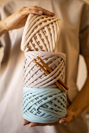 Female hands holding stack of hank reels multicolored ribbon yarn and wooden crochet needle
