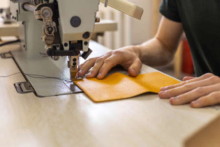 Close up craftsman hands sew stuff blank for wallet use sewing machine. Working at leather workshop
