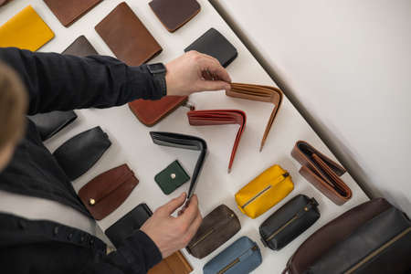Craftsman hands laying out leatherwork on wooden showcase at leather workshop. Handwork accessories
