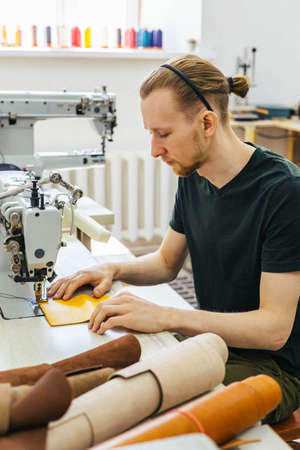 Close up craftsman hands sew stuff blank for wallet use sewing machine. Working at leather workshopの写真素材
