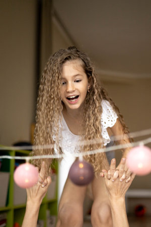 Happy curly baby girl holding grandmother hands playing illuminated ball garland positive emotion