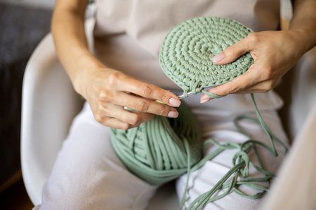 Closeup female hands knitting interior decor basket use green ribbon yarn and crochet needleの写真素材