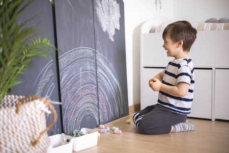 Cute baby boy drawing on black chalkboard colorful chalks indoor at childish playroom kindergartenの写真素材