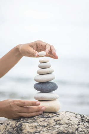 Tanned woman hands stacked pebble stones tower on sea beach relaxing harmony summer travel vacationの写真素材