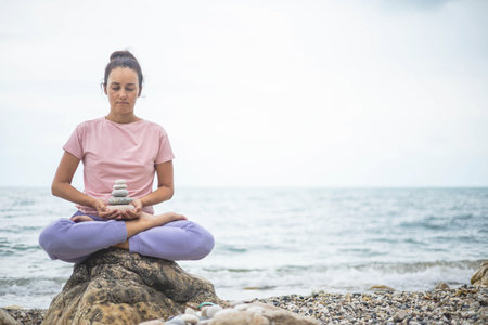 Spiritual yoga woman lotus position on cobblestone with pebble tower harmony relax meditation beachの写真素材