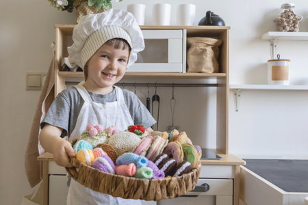 Cute little baby boy in chef hat and apron playing at childish kitchen cooking food back view