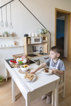 Cute little baby boy in chef hat and apron playing at childish kitchen cooking food back viewの写真素材