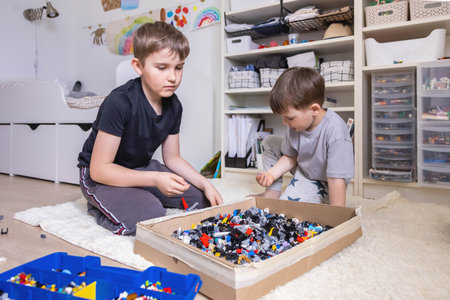 Khabarovsk, Russia, June 4, 2022. Two male kid playing Lego pieces on floor at childish roomのeditorial素材