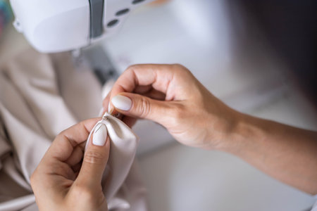 Female tailor hands sewing beige textile with needle and thread process of clothes handmade creating