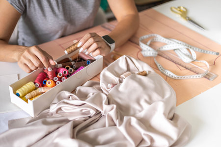 Woman dressmaker hands choosing thread color sewing beige fabric clothes at workshop studio closeupの写真素材