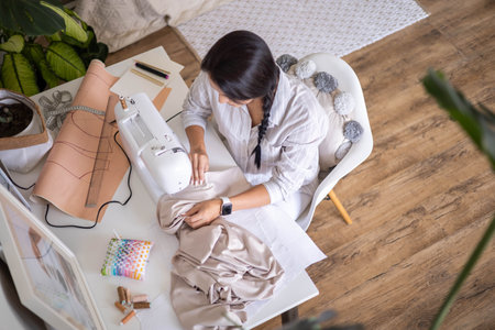 Female skilled dressmaker sews fabric garment on sewing machine enjoy work at home workplaceの写真素材