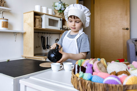 Cute little baby boy in chef hat and apron playing at childish kitchen cooking food back viewの写真素材