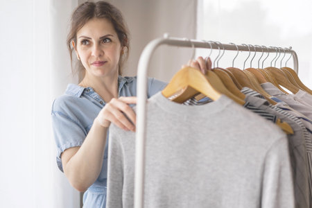 Young beautiful woman stands near the closet and hangs up her clothes. Clothes storage.