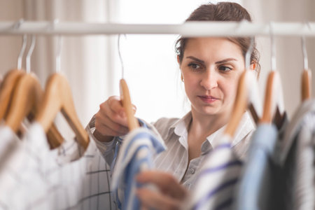 Young beautiful woman stands near the closet and hangs up her clothes. Clothes storage.の写真素材