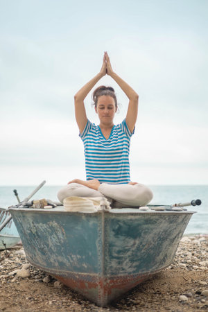 Meditative woman sitting lotus position at boat on sand beach sea landscape travel harmony balanceの写真素材