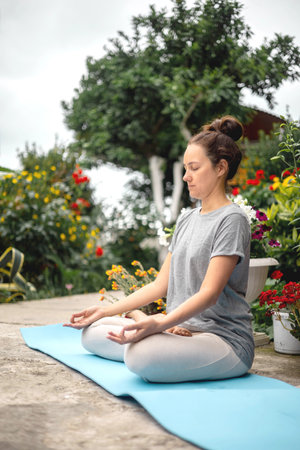 Concentrated woman sitting in lotus position yoga at summer garden park plants and blossom flowers