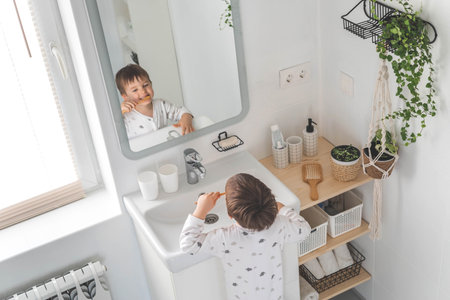 Cute male kid in pajamas cleaning teeth with eco friendly toothbrush comfortable minimalist bathroomの写真素材