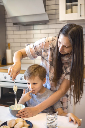 Mom and children prepare icing for gingerbread in their home kitchen. Beat with a blender. The girl helps the woman.の写真素材