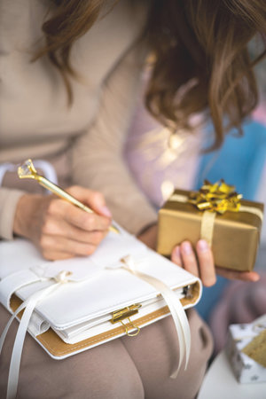 Closeup female hands writing Christmas festive congratulations on card for gift box packageの写真素材
