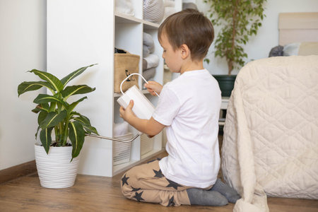 Little cute boy is watering indoor plants from a stylish watering can in a designer home interior.の写真素材