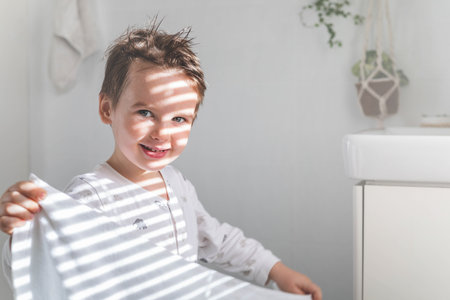 Morning baby boy wiping face white soft towel after washing at domestic bathroom sunlight closeupの写真素材