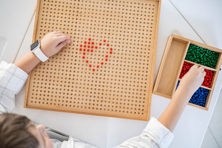 Boy child use multiplication Montessori wooden board with red beads heart shape on deskの写真素材
