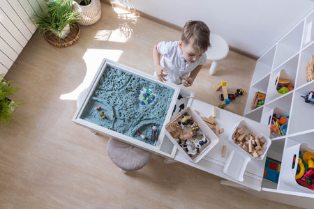 Cute baby boy playing sensory box kinetic sand table with farm animalsの写真素材