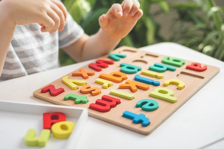 Male kid playing with wooden eco friendly alphabet letters board on table top view intellectual gameの写真素材