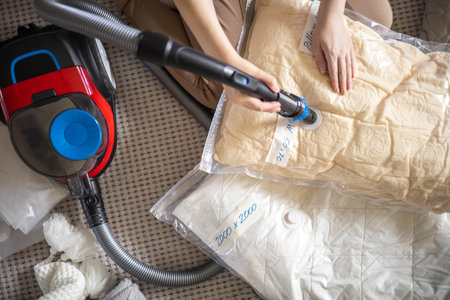 The girl pumps out air with a vacuum cleaner from a vacuum bag with clothes. The concept of storage and transportation of clothing, things. Space saving seal bag.の写真素材