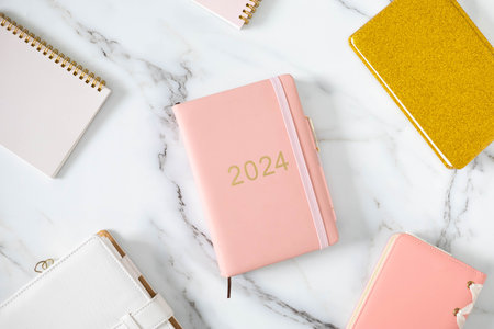 Pink coral colored diary for the year 2024 and many other diaries, pen, marble backgroundの写真素材