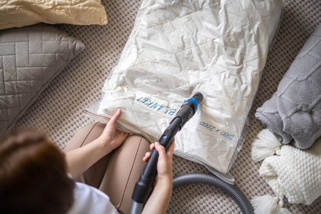 The girl pumps out air with a vacuum cleaner from a vacuum bag with pillow and blanket. The concept of storage and transportation of clothing, things. Space saving seal bag.の写真素材
