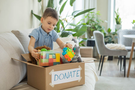 Boy child puts toys in a cardboard box for charity. Donation concept.
