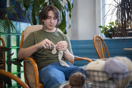 Feminine hipster man crochet handmade use hook knitting needles and wool yarn relaxing on couchの写真素材