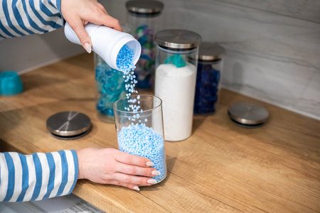 Female housewife hands sprinkle dry blue granular laundry conditioner glass can storage organizing