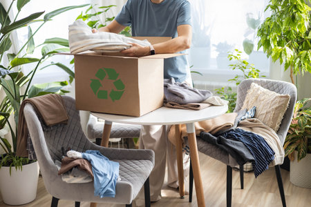 Recycling concept. A woman at home collects clothes in a box for recycling or disposal.