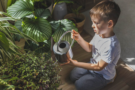 A child in home clothes waters indoor plants from a beautiful stylish metal watering can.の写真素材