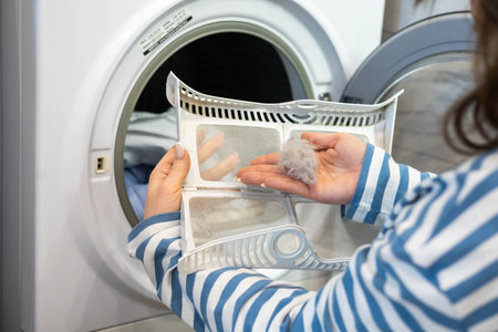Female housewife hands cleaning filter dryer machine from wool textile fiber and particles closeupの写真素材