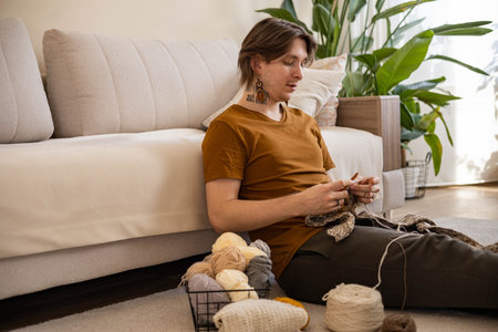 Feminine hipster man crochet handmade use hook knitting needles and wool yarn relaxing on couch