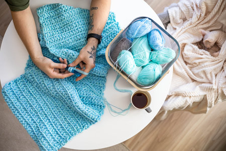 Male hands crochet handmade artwork use wool yarn and hook over table with coffee