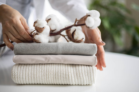 Womens hands hold a stack of neat, clean, cotton clothes in neutral shades. Branch with cotton...