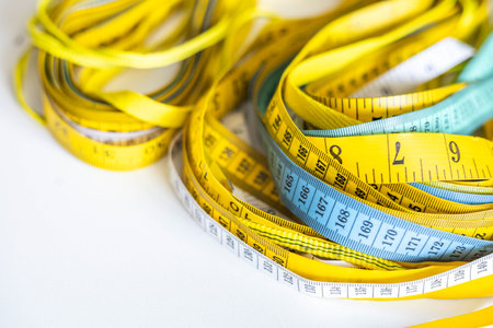 A lot of multi-colored centimeter and inch measuring tapes lie on a white background on the table.